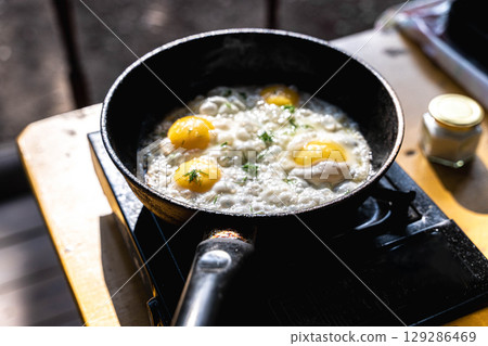 Fried eggs cooking in a pan on a portable stove Fried eggs cooking in a pan on a portable stove 129286469