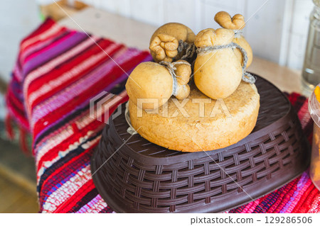 Caciocavallo podolico cheese resting on a wheel of cheese in a basket on a colorful tablecloth 129286506