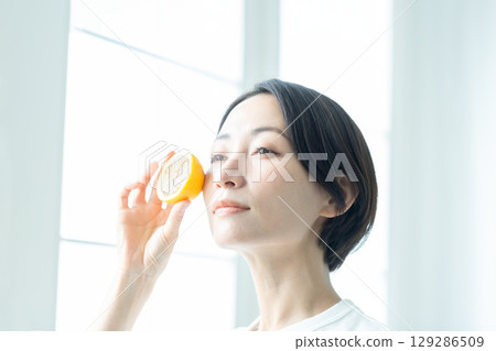 A woman with a translucent look holding a lemon by the window, close-up of her face 129286509