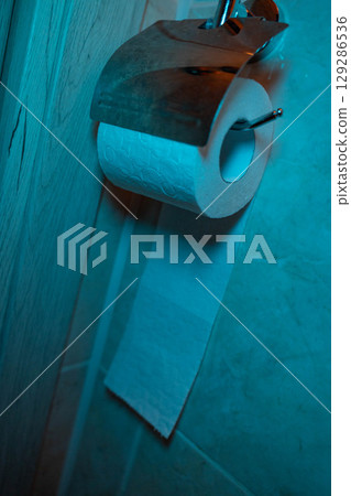 Toilet paper hanging on a holder in a bathroom with blue lighting 129286536