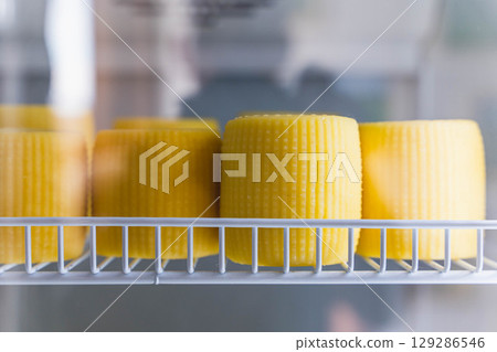 Fresh cheese wheels ripening in refrigerator display case 129286546
