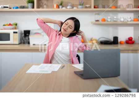Home Office. Young woman relieving neck tension during remote work. 129286798