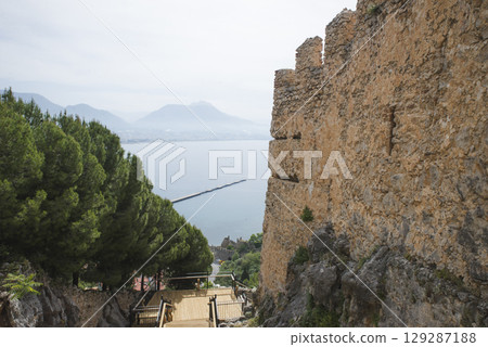 Awesome view of the Kizil Kule (Red Tower) from fortress walls of Alanya Castle in Turkey. The Mediterranean Sea is visible in background. The octagonal red brick tower is a popular tourist attraction 129287188