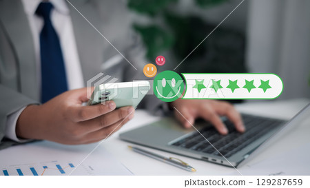 Concept for positive customer experience, service quality, and business satisfaction. Business person giving five-star rating with happy emoji on smartphone. 129287659