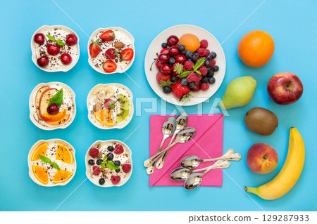 6 bowls of differently dressed yogurts displayed vertically in 2 rows of 3 pc. near plate of berries, fruits, 6 spoons, napkins on blue background. Six yogurts ready to eat and ingredients. Top view. 6 bowls of differently dressed yogurts displayed vertically in 2 rows of 3 pc. near plate of berries, fruits, 6 spoons, napkins on blue background. Six yogurts ready to eat and ingredients. Top view. 129287933
