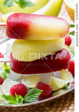 Column of melon lime raspberries sorbet ice cream. Delicious melon raspberry ice cream is displayed on a silver tray, surrounded by ice, fresh raspberries, lime slices, and mint leaves Column of melon lime raspberries sorbet ice cream. Delicious melon raspberry ice cream is displayed on a silver tray, surrounded by ice, fresh raspberries, lime slices, and mint leaves 129287950