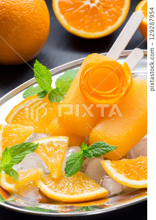 Vibrant orange icecream sits on a silver platter accompanied by fresh orange slices and mint leaves, creating a refreshing dessert perfect for hot summer days. Vibrant orange icecream sits on a silver platter accompanied by fresh orange slices and mint leaves, creating a refreshing dessert perfect for hot summer days. 129287954