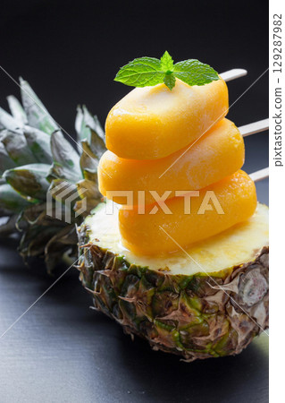 Column of sorbet ice cream popsicles from pineapple on half of pineapple on a black background. Pineapple sorbet ice cream popsicles. Vertical. Close. Column of sorbet ice cream popsicles from pineapple on half of pineapple on a black background. Pineapple sorbet ice cream popsicles. Vertical. Close. 129287982