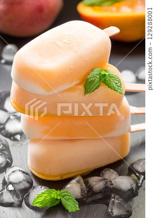 Three mango ice cream popsicles are piled on top of each other on a dark surface. They are surrounded by ice cubes, suggesting a refreshing treat perfect for a warm summer day. Three mango ice cream popsicles are piled on top of each other on a dark surface. They are surrounded by ice cubes, suggesting a refreshing treat perfect for a warm summer day. 129288001