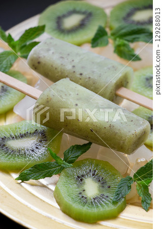 Delicious kiwi icecream popsicles are placed on a round, decorative plate surrounded by fresh kiwi slices and vibrant mint leaves, creating a refreshing treat perfect for warm weather. Delicious kiwi icecream popsicles are placed on a round, decorative plate surrounded by fresh kiwi slices and vibrant mint leaves, creating a refreshing treat perfect for warm weather. 129288013