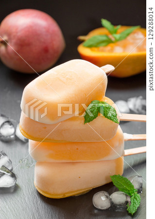Column of 4 mango sorbet sundae mix ice cream behind mango and cutted mango near ice cubes on a black background. Mango sorbet sundae mix ice cream popsicles. Vertical. Column of 4 mango sorbet sundae mix ice cream behind mango and cutted mango near ice cubes on a black background. Mango sorbet sundae mix ice cream popsicles. Vertical. 129288014