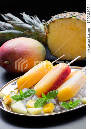 Mango pineapple ice cream popsicles arranged on a decorative plate with crushed ice and fresh fruit. A ripe mango and a halved pineapple enhance the tropical theme. Mango pineapple ice cream popsicles arranged on a decorative plate with crushed ice and fresh fruit. A ripe mango and a halved pineapple enhance the tropical theme. 129288054