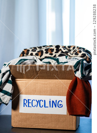 Woman prepared cardboard box full of used outfits for recycling. Responsible disposal and secondhand fashion concept. 129288238