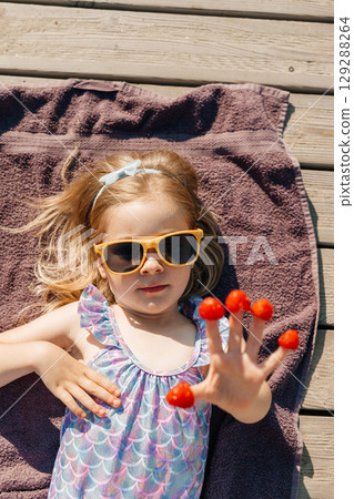 Child relaxing outdoors with sunglasses and raspberries on fingers during sunny day 129288264