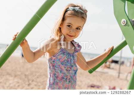 Young girl enjoys playing on playground equipment during sunny beach day Young girl enjoys playing on playground equipment during sunny beach day 129288267