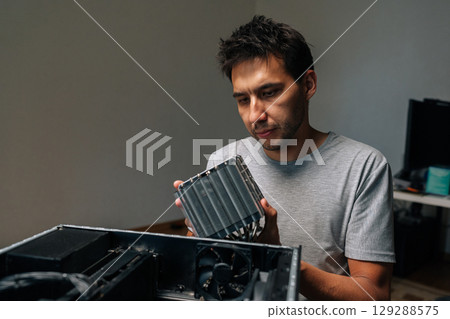 Portrait of computer technician installing cooling radiator, carefully positioning computer hardware component during precision workstation maintenance. Concept of desktop PC maintenance and service. 129288575
