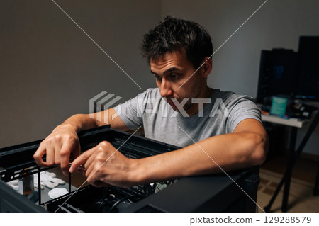 Focused technician male inserting processor into desktop motherboard during computer hardware upgrade or repair process at dark workshop. Concept of desktop PC maintenance and service. 129288579