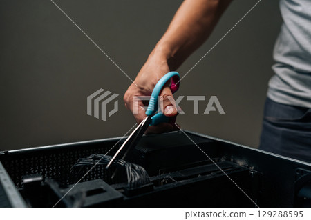 Close-up of technician hand using scissors to cut cable inside desktop computer, performing maintenance or repair work on complex internal components. Concept of desktop PC service. Close-up of technician hand using scissors to cut cable inside desktop computer, performing maintenance or repair work on complex internal components. Concept of desktop PC service. 129288595