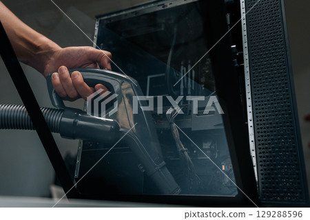 Close-up of technician using vacuum cleaner to remove dust and debris from inside computer case, performing essential maintenance for optimal performance. Concept of service, cleaning computer. Close-up of technician using vacuum cleaner to remove dust and debris from inside computer case, performing essential maintenance for optimal performance. Concept of service, cleaning computer. 129288596
