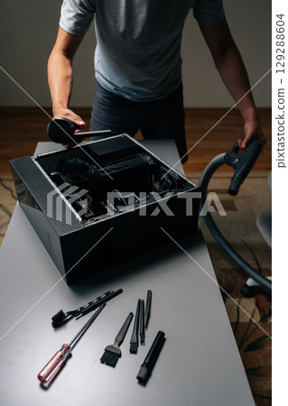 Vertical shot of computer repair professional cleaning computer interior with vacuum preventing dust accumulation and potential hardware damage. Servicing motherboard of dusty computer at workshop. 129288604