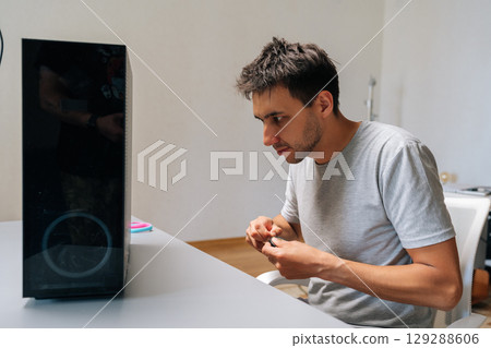 Puzzled technician male applying black electrical tape while performing computer case repair, showing diy troubleshooting technique at workshop. Concept of desktop PC maintenance and service. 129288606