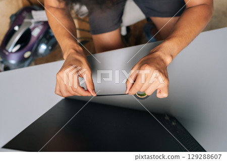 High-angle view of technician applying piece of black electrical tape to edge of computer case, engaged in diy repair at home, demonstrating skill and resourcefulness in technology maintenance. 129288607