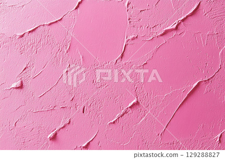A close-up of a weathered, cracked wall with peeling paint, showing a textured surface in various shades of pink and light purple. 129288827