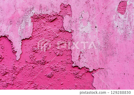 A close-up of a weathered, cracked wall with peeling paint, showing a textured surface in various shades of pink and light purple. 129288830