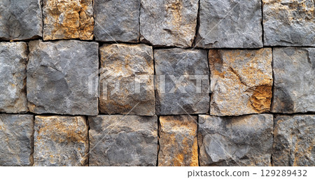 A close-up view of a stone wall made of variously shaped and colored stones, showcasing a rustic and textured appearance. 129289432