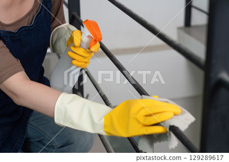 Home Cleaning. Close-up of young woman cleaning railing with spray cleaner. 129289617