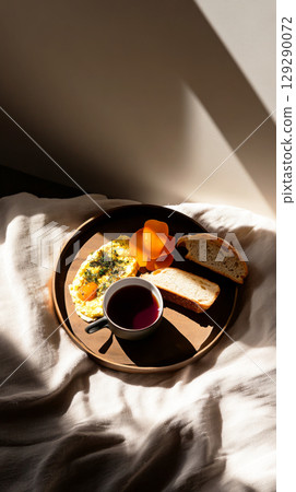 Bright morning light filters through as breakfast is served, featuring fluffy eggs, fresh bread, and a warm cup of tea, creating a serene and comforting start to the day 129290072