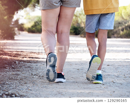 Woman walking hand in hand with her son through a green park pathway Woman walking hand in hand with her son through a green park pathway 129290165