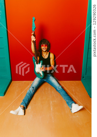 A man is holding a guitar and is sitting on the floor A man is holding a guitar and is sitting on the floor 129290326