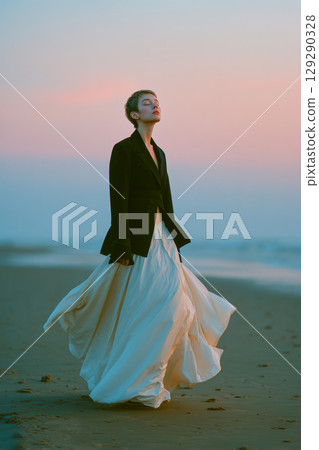 A woman is standing on a beach wearing a black jacket and a white skirt A woman is standing on a beach wearing a black jacket and a white skirt 129290328