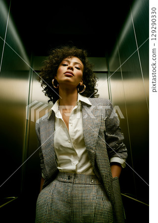 A woman in a black and white checked jacket and pants poses in an elevator 129290330