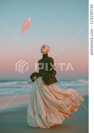 A woman is standing on a beach, wearing a long skirt and a black jacket 129290336