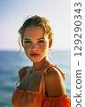 A woman with blonde hair and a red dress is standing on a beach 129290343