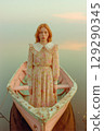 A woman in a floral dress stands in front of a boat 129290345