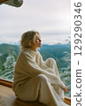 A woman is sitting in a room with a view of mountains 129290346