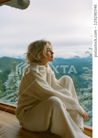 A woman is sitting in a room with a view of mountains A woman is sitting in a room with a view of mountains 129290346