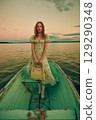 A woman in a yellow dress is posing in a boat on a lake 129290348