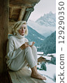 A woman in a white sweater and white pants is sitting on a wooden deck 129290350
