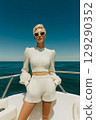 A woman in a white outfit is posing on a boat in the ocean 129290352