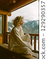A woman in a white sweater sits on a wooden bench looking out at the mountains 129290357