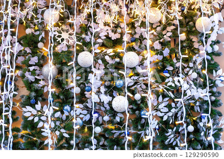 Christmas decorated wall with green fir branches illuminated, white artificial leaves and balls 129290590