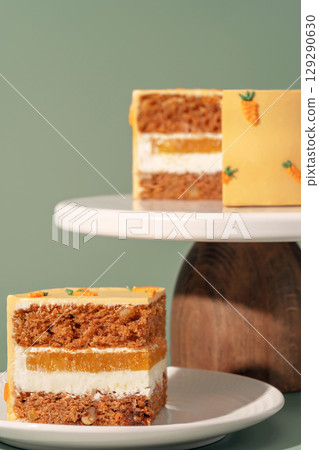 Bento cake featuring layers of carrot, orange, and mango, beautifully presented on a white cake stand against a soft green background, showcasing vibrant colors and textures for dessert lovers Bento cake featuring layers of carrot, orange, and mango, beautifully presented on a white cake stand against a soft green background, showcasing vibrant colors and textures for dessert lovers 129290630