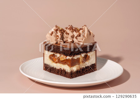 Caramel and nut bento cake with chocolate sponge layers, topped with creamy frosting and chocolate shavings, presented on a white plate against a soft pastel background, dessert concept 129290635