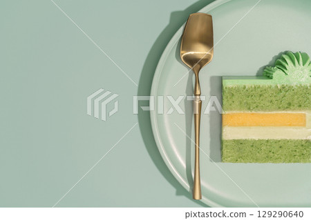 Colorful bento cake featuring layers of mango and passion fruit, pistachio sponge, elegantly presented on a pale plate with a golden serving utensil, showcasing a delightful dessert concept 129290640