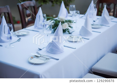 Festively laid table with white tablecloths glasses and plates Festively laid table with white tablecloths glasses and plates 129290878