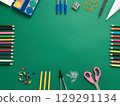 Colorful school supplies arranged on a green background. Items include colored pencils, scissors, paper clips,  129291134